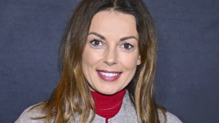 Katarzyna Glinka w czerwonej sukience i szarej kurtce, w rozpuszczonych włosach i czerwonej szmince