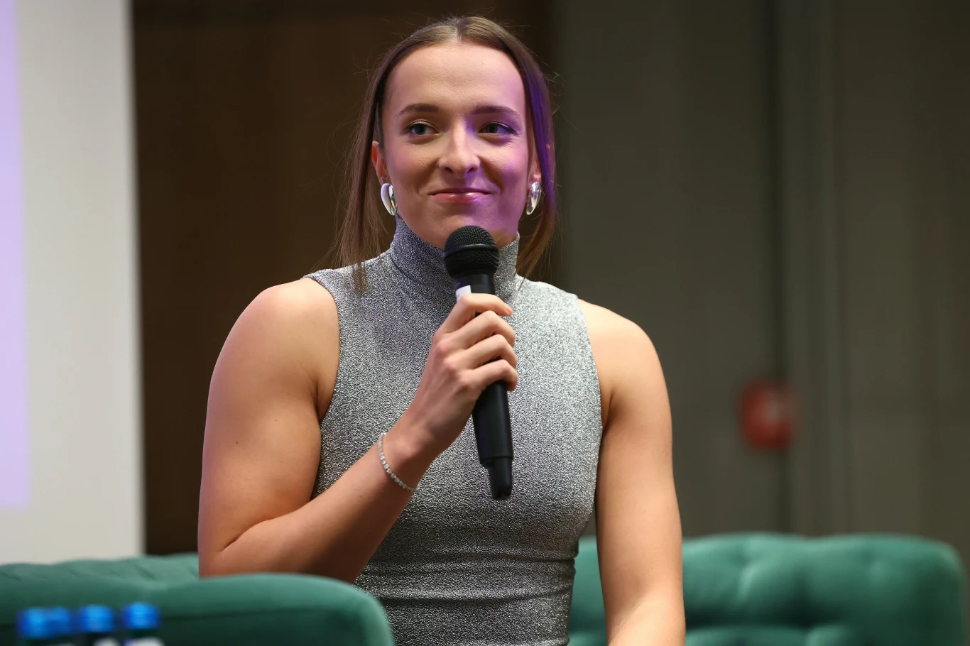 Iga Świątek powołała do życia fundację swojego imienia Kobieta w sportowym stroju siedzi na zielonej kanapie, trzyma mikrofon w dłoni i uśmiecha się lekko w stronę publiczności. W tle rozmyty fragment sali konferencyjnej.