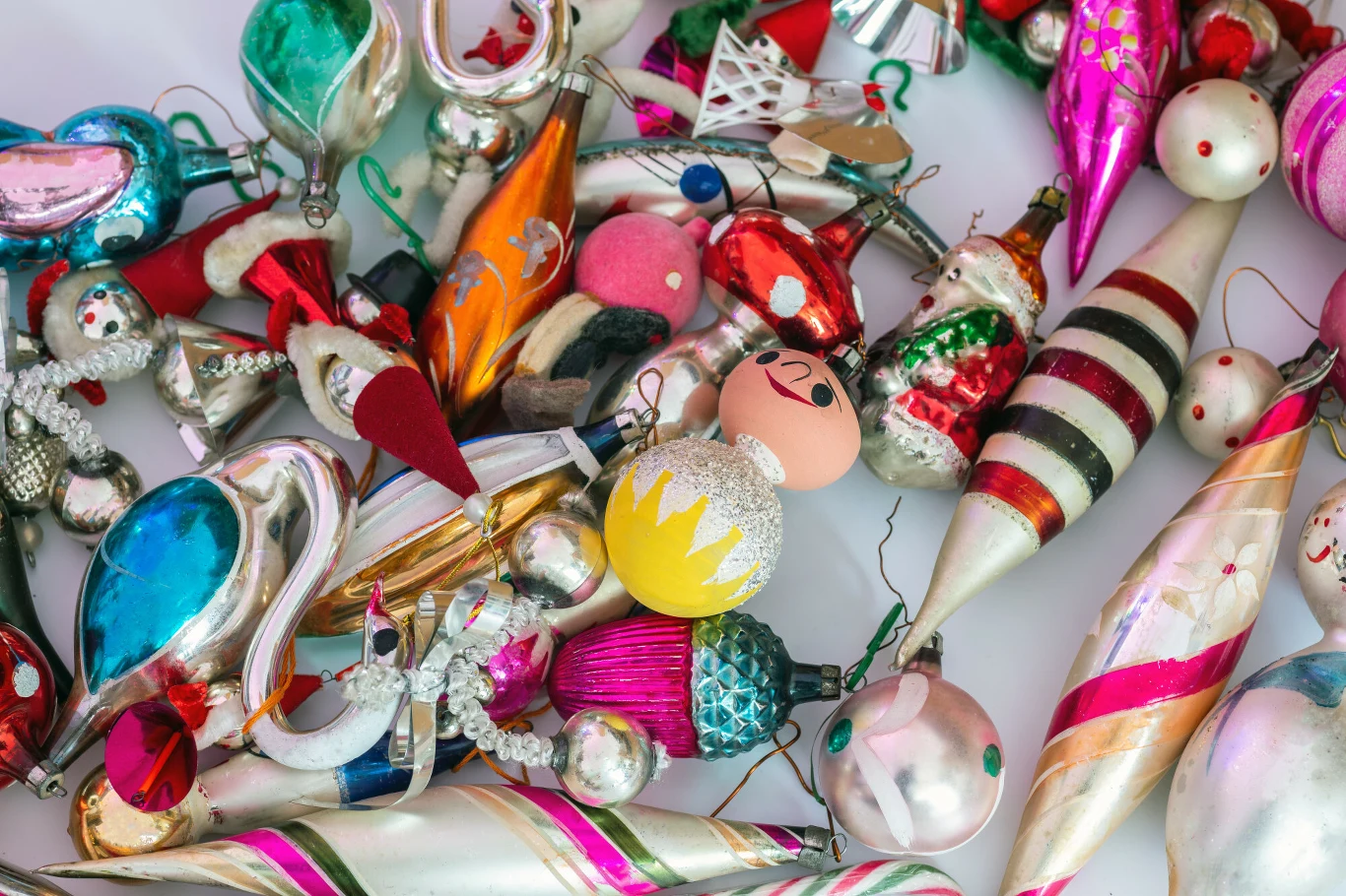 Różnorodne kolorowe szklane bombki choinkowe o różnych kształtach i wzorach, w tym ozdoby w kształcie stożków, kul i postaci, połyskujące metalicznymi i pastelowymi barwami.