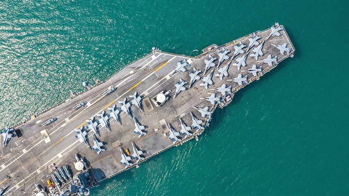 USA kończą budowę najpotężniejszego lotniskowa atomowego świata - USS John F. Kennedy (CVN-79) Lotniskowiec płynący po morzu z rozmieszczonymi równomiernie na pokładzie samolotami odrzutowymi, otoczony spokojną, turkusową wodą. Pokład jest w pełni wyposażony i gotowy do operacji.