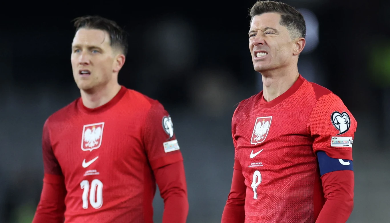 Piotr Zieliński i Robert Lewandowski mają świadomość, że do finałów MŚ jeszcze daleka droga Dwóch piłkarzy w czerwonych koszulkach polskiej reprezentacji piłkarskiej stoi obok siebie na boisku, jeden z nich ma opaskę kapitana i wyraz grymasu na twarzy, drugi zachowuje spokojny wyraz twarzy.