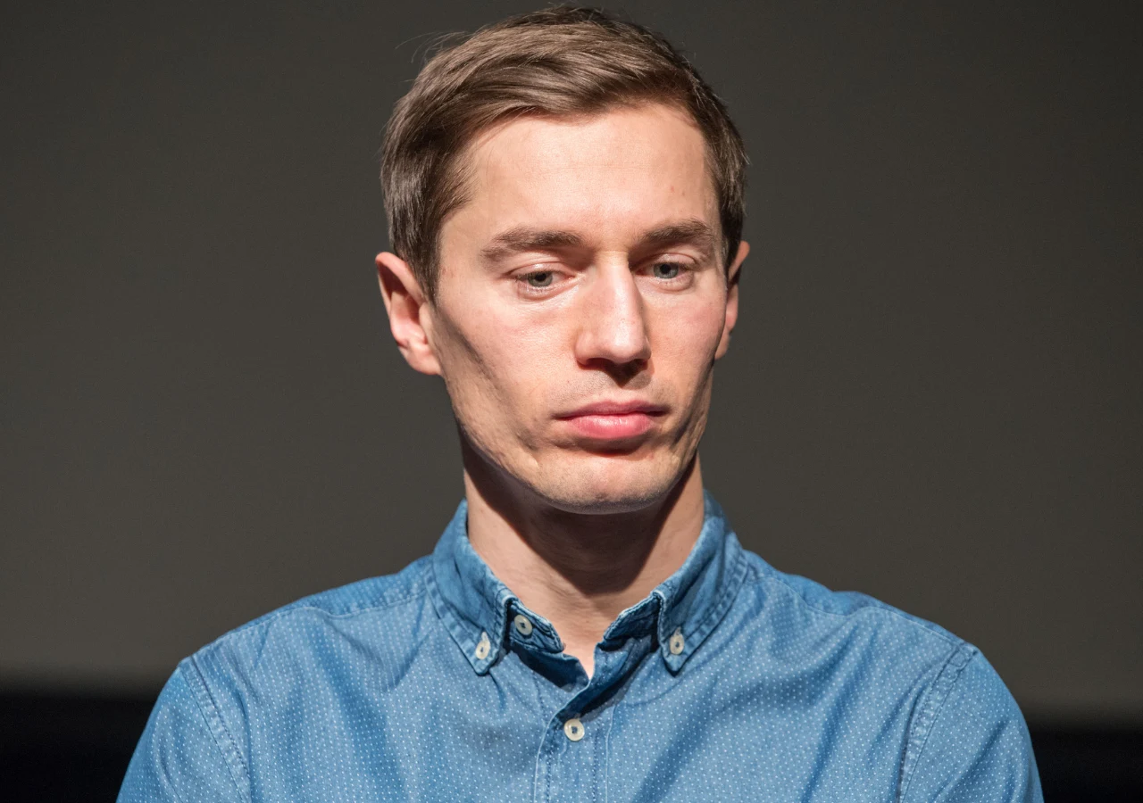 Kamil Stoch Mężczyzna o jasnych włosach ubrany w niebieską koszulę patrzy poważnie w dół, na neutralnym, ciemnym tle.