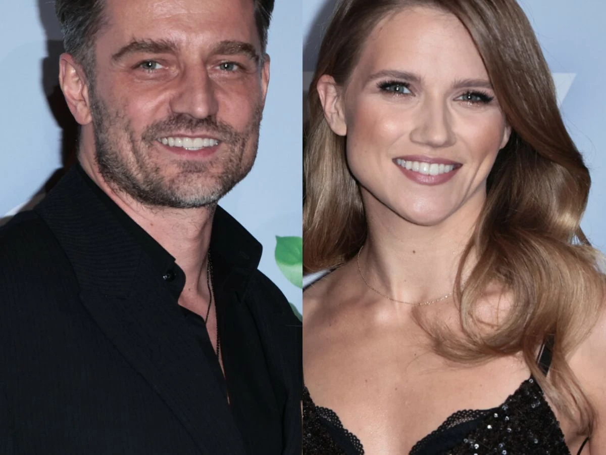 Marcin Rogacewicz, Agnieszka Kaczorowska Dwie uśmiechnięte osoby, mężczyzna w ciemnej marynarce i kobieta z długimi, jasnobrązowymi włosami w czarnej, eleganckiej sukience, stoją na tle jasnoniebieskiej ścianki z elementami zieleni.