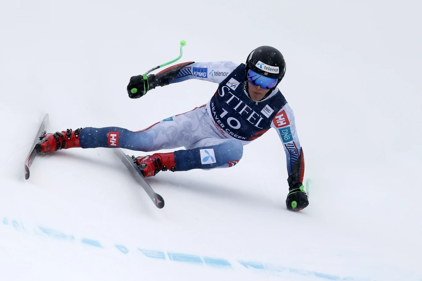 Narciarz alpejski w stroju wyścigowym z numerem 10 dynamicznie pokonuje zakręt na trasie zjazdowej, intensywnie pochylając się ku śnieżnemu podłożu.