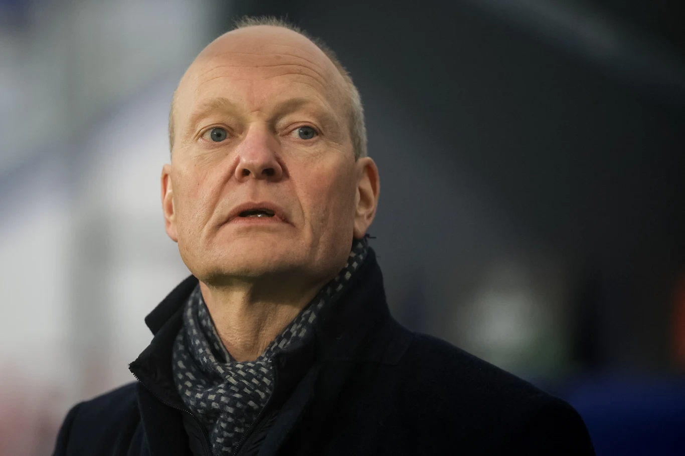 Niels Frederiksen, Ołomuniec 2035 Łysy mężczyzna w średnim wieku ubrany elegancko w ciemny płaszcz i szalik w kratę na tle rozmytego, neutralnego tła.