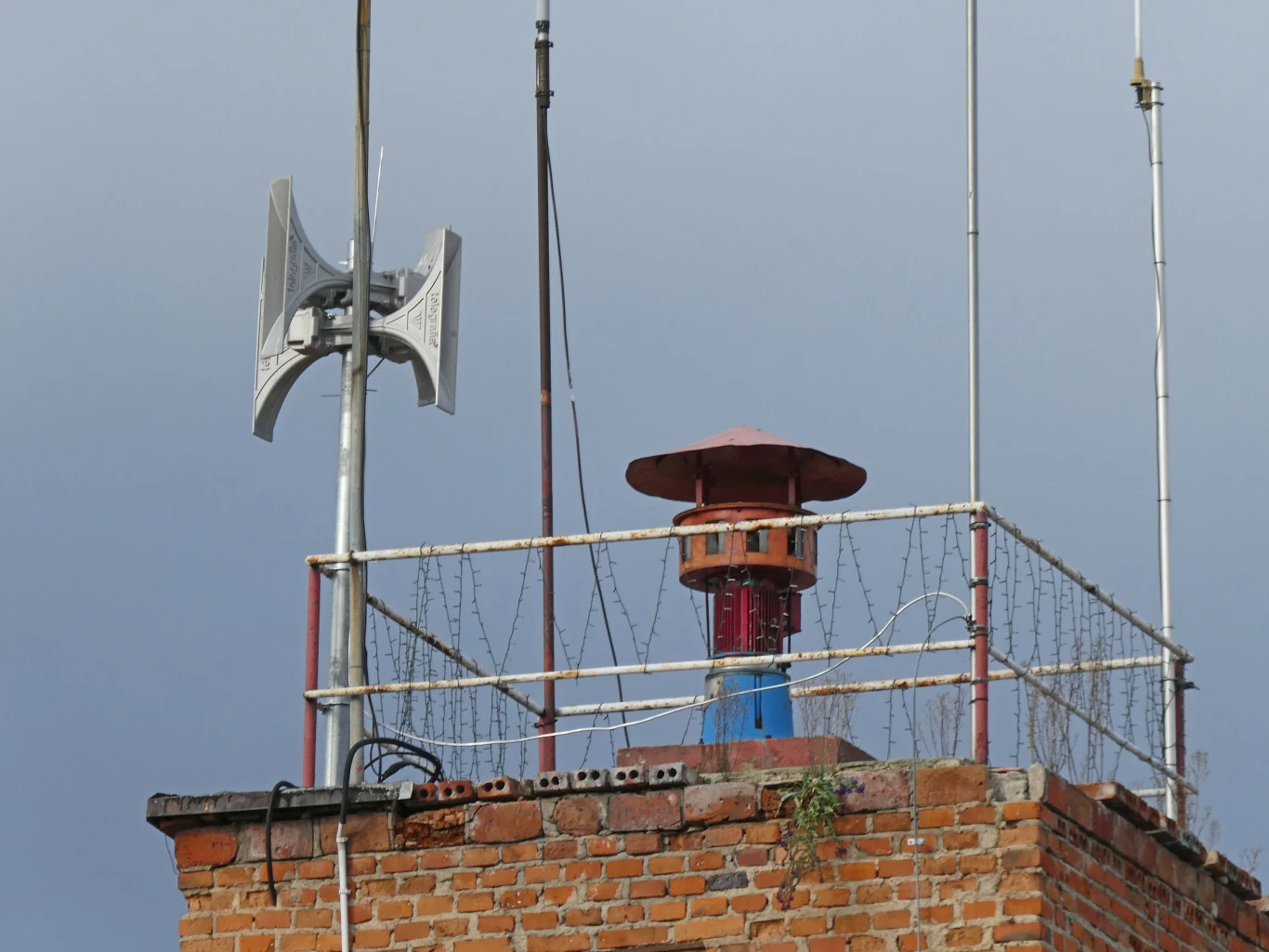 Syreny alarmowe wyją zbyt często. Samorządowcy chcą zmian w obliczu wojny za wschodnią granicą Syrena alarmowa oraz głośnik zamontowane na szczycie ceglanego budynku, otoczone metalową barierką i drutem kolczastym, tło stanowi jasne niebo.