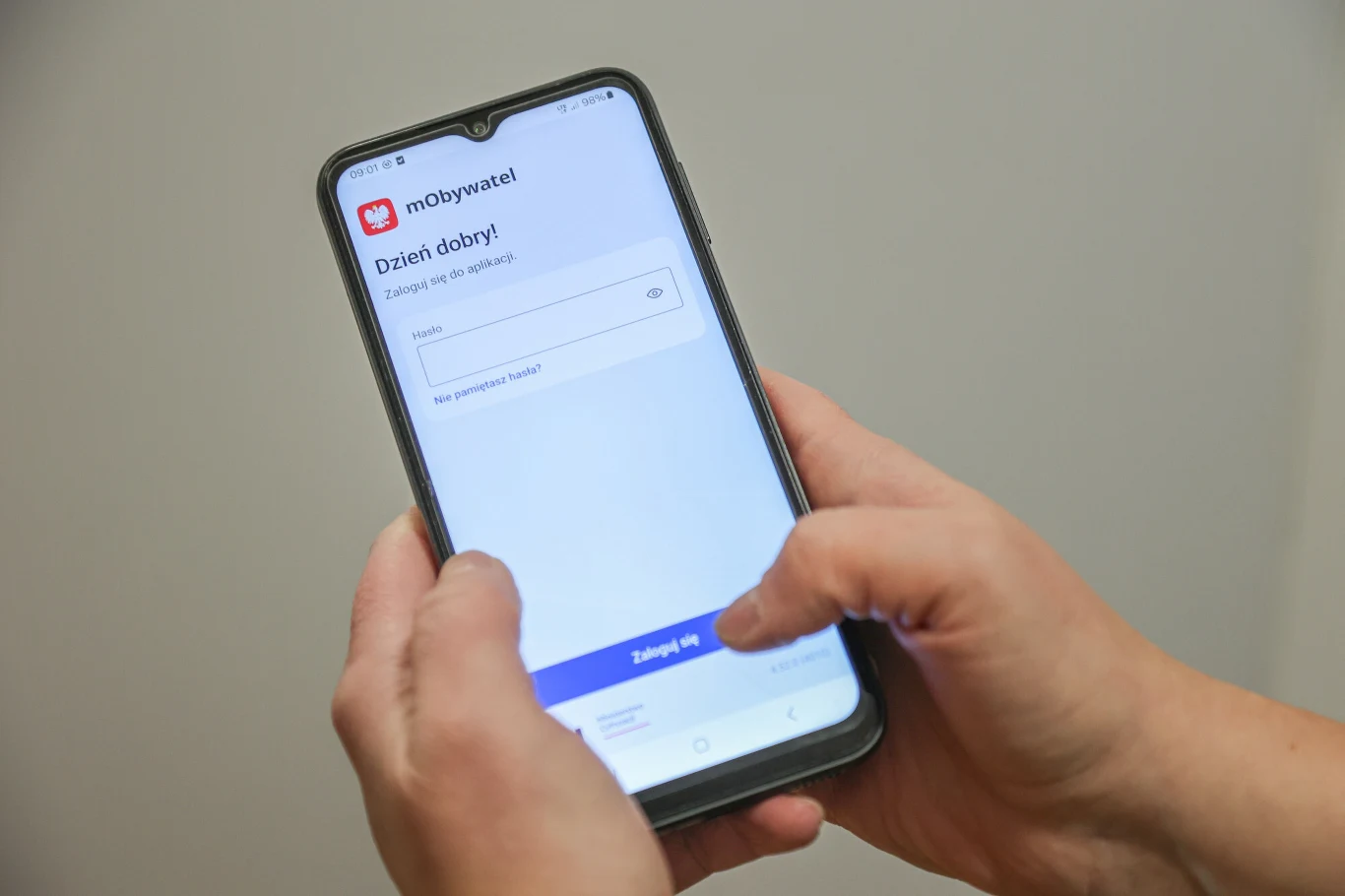 Ekran smartfona trzymanego w dłoniach, na którym widać uruchomioną aplikację mObywatel z polem do wpisywania loginu i hasła oraz przyciskiem zaloguj się.