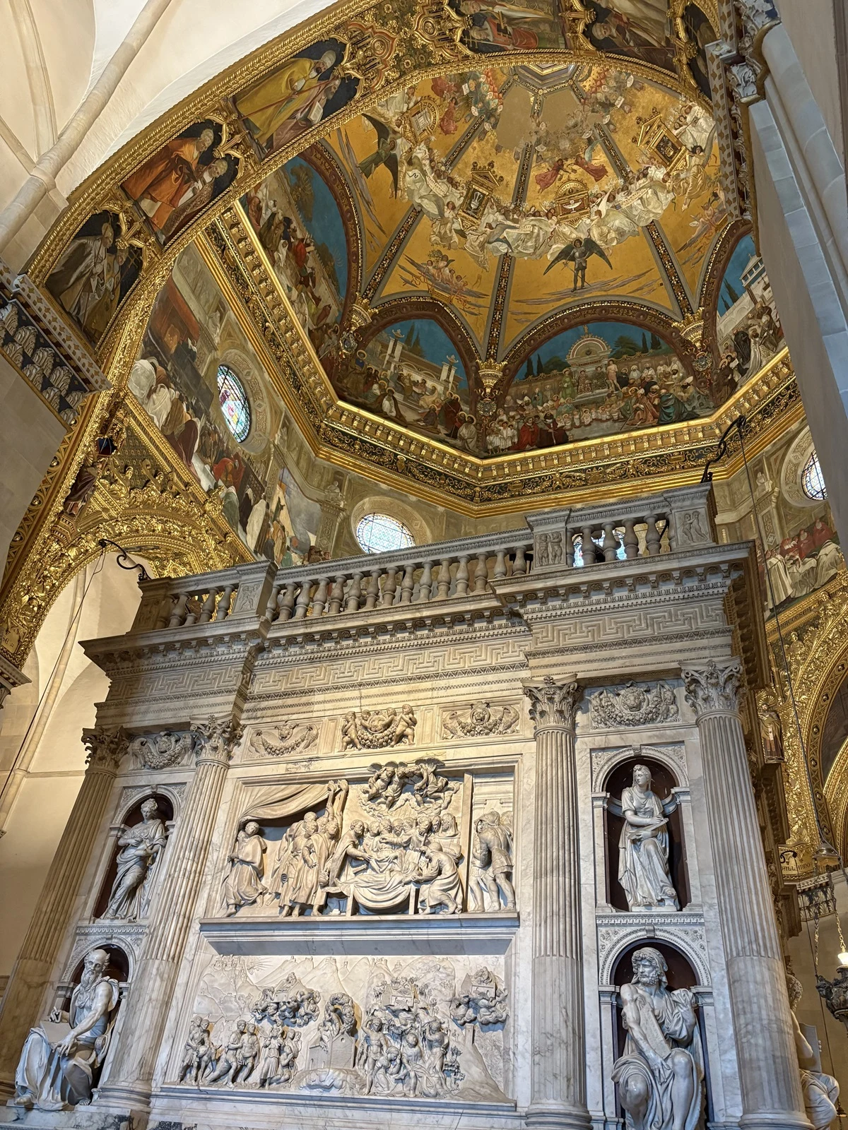 Monumentalny grobowiec dekorowany licznymi płaskorzeźbami, otoczony rzeźbionymi postaciami świętych, w tle złocony, misternie zdobiony sufit pokryty freskami o tematyce religijnej.