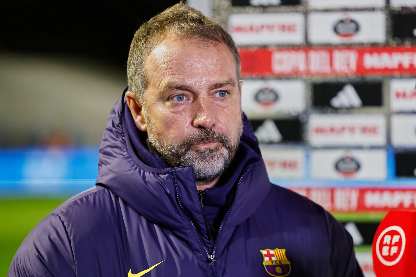 Mężczyzna ubrany w kurtkę z herbem FC Barcelony stoi na tle ścianki sponsorsko-medialnej podczas wywiadu lub konferencji prasowej.