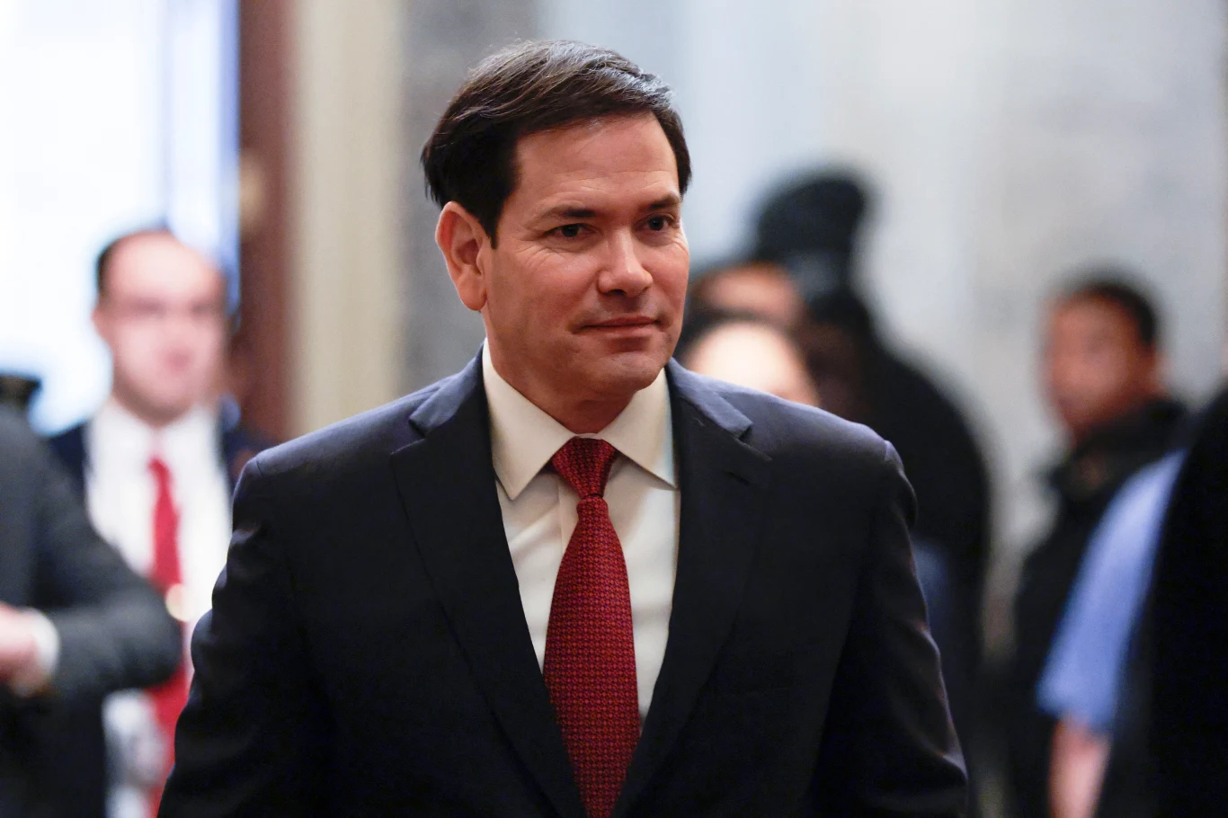 Marco Rubio nie obawia się eskalacji konfliktu z Rosją w związku z działaniami wobec Wenezueli Mężczyzna w garniturze i czerwonym krawacie stoi w otoczeniu innych osób, rozmytych w tle. Wygląda na skupionego i poważnego, znajduje się w jasnym wnętrzu.