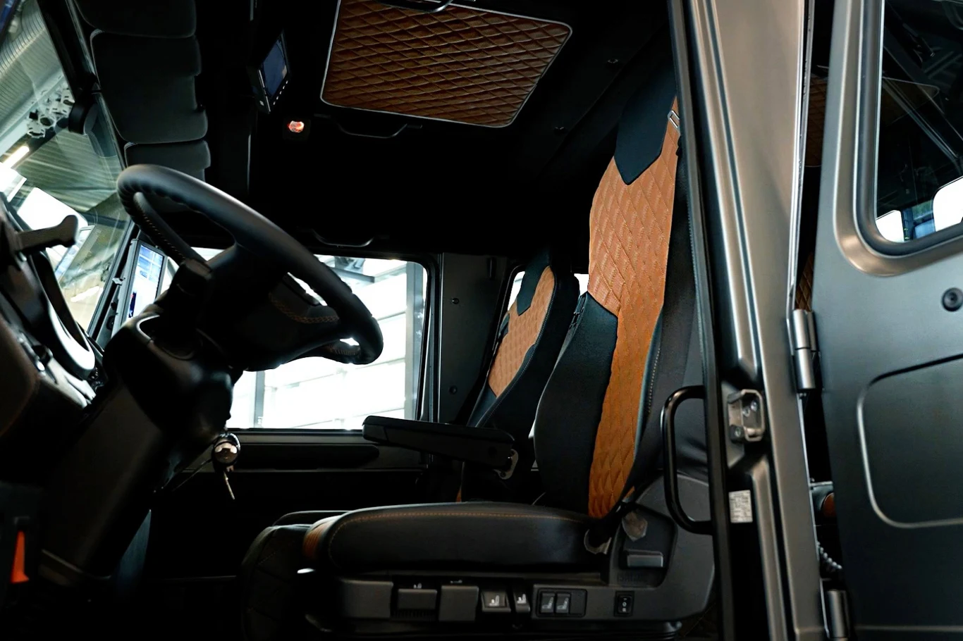 Wnętrze nowoczesnej kabiny pojazdu ciężarowego z widocznymi skórzanymi fotelami w kolorze brązowo-czarnym, kierownicą oraz deską rozdzielczą.