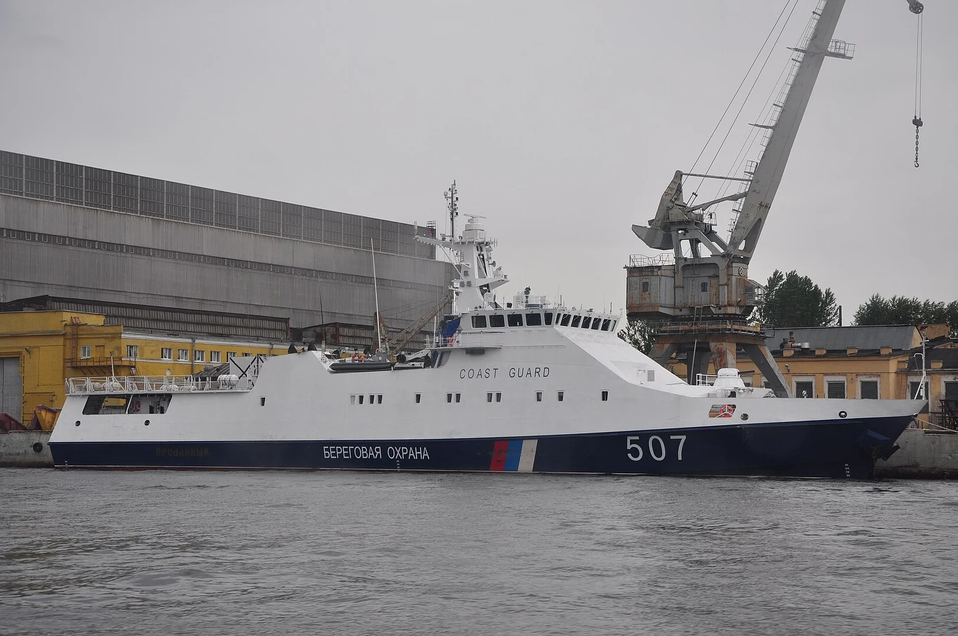 Statek straży przybrzeżnej o numerze 507 zacumowany przy nabrzeżu, w tle widoczny dźwig portowy, budynki przemysłowe oraz elementy portowej infrastruktury.