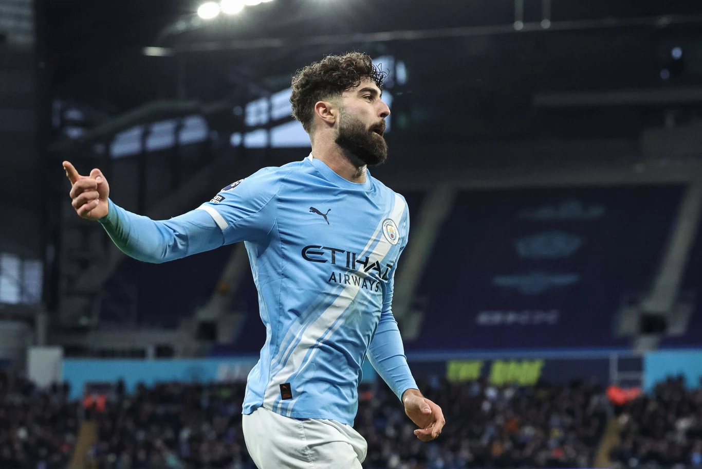 Piłkarz w stroju Manchester City świętuje zdobycie bramki podczas meczu na stadionie, w tle widoczna publiczność i trybuny.