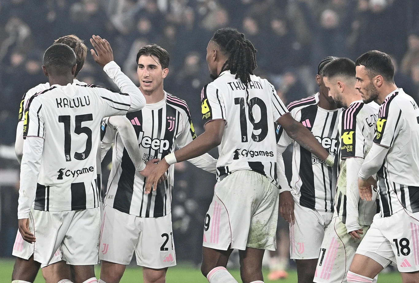 Piłkarze Juventusu Zawodnicy drużyny piłkarskiej Juventus celebrują wspólnie na boisku po zdobyciu bramki, ubrani w czarno-białe stroje z widocznymi numerami i nazwiskami, otoczeni kibicami na trybunach.
