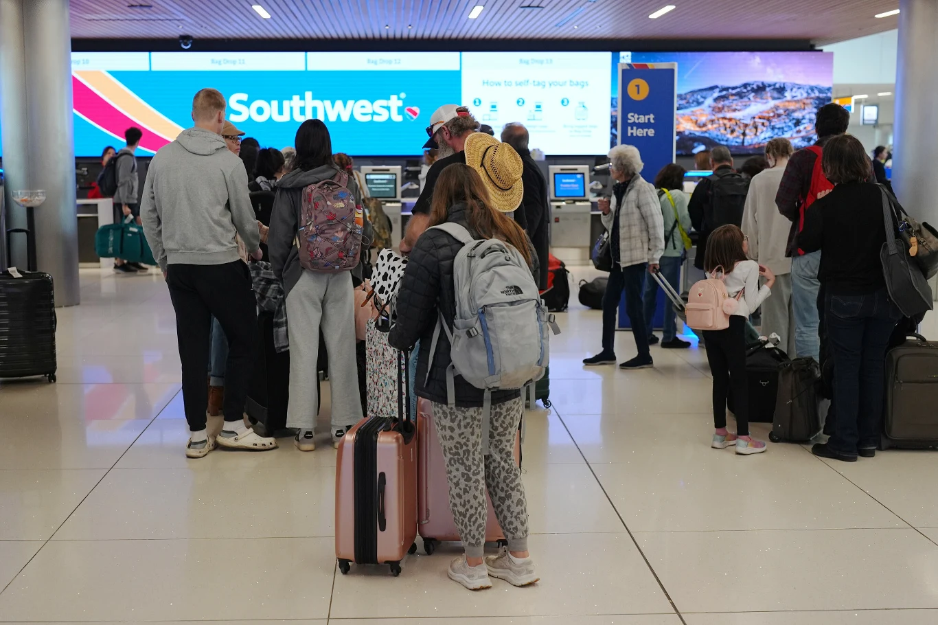 Southwest Airlines wprowadza nową politykę. Osoby z otyłością będą musiały wykupić dwa miejsca. Grupa podróżnych stoi w kolejce przy stanowisku odpraw lotniczych Southwest Airlines, większość osób z walizkami i plecakami, po lewej stronie widoczny podświetlany ekran z logo linii lotniczych.