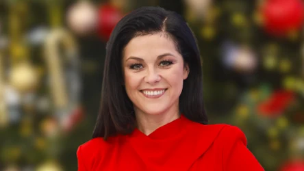 Uśmiechnięta Kasia Cichopek w czerwonej sukience na tle choinki