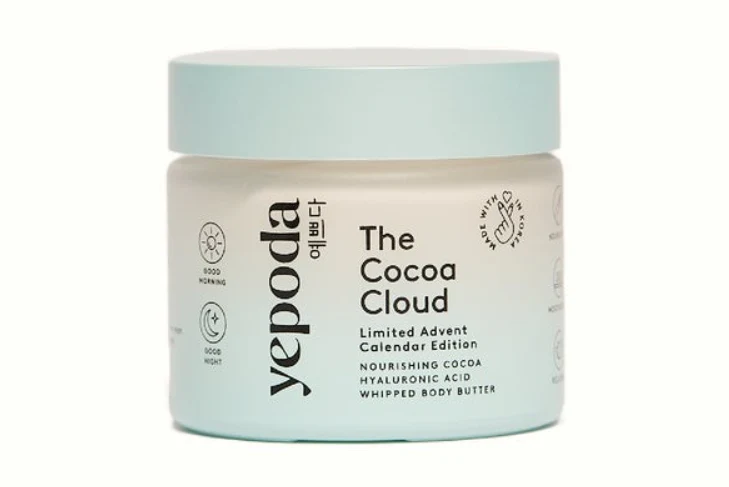 Biały słoik z błękitną nakrętką, na którym widnieje napis 'yepoda The Cocoa Cloud Limited Advent Calendar Edition Nourishing Cocoa Hyaluronic Acid Whipped Body Butter'. Opakowanie utrzymane w minimalistycznej stylistyce, z graficznymi detalami i subtel...