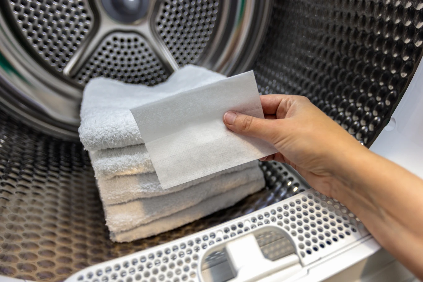 Triki na czystą kanapę Ręka trzymająca arkusz papieru do suszarki, wkłada go do bębna pralki z ułożonymi białymi, czystymi ręcznikami.