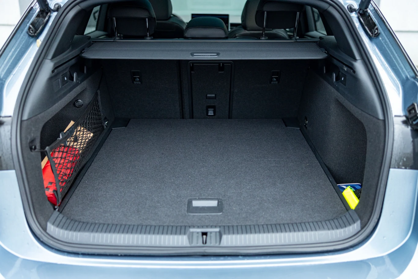 Bagażnik Id.7 w wersji Tourer ma aż 605 litrów pojemności Pojemny bagażnik samochodu osobowego z gładką wykładziną, siatką na akcesoria po lewej stronie, widocznymi drobnymi przedmiotami oraz złożonymi tylnymi siedzeniami.