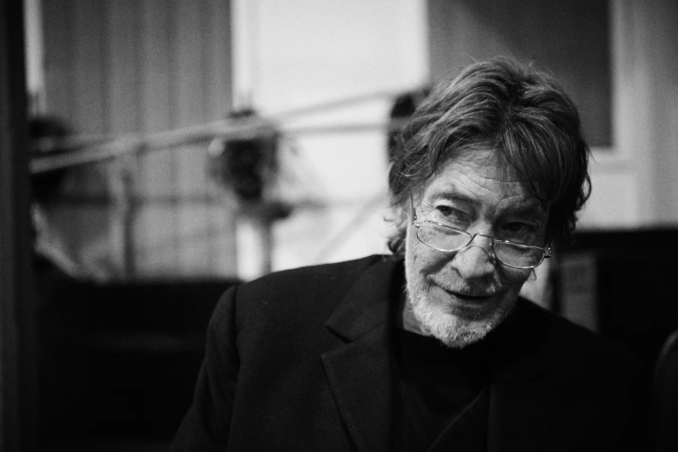 Chris Rea w 2015 r. Starszy mężczyzna z brodą i okularami w ciemnej marynarce, patrzący lekko na bok. Tło rozmyte, wnętrze pomieszczenia o neutralnym charakterze.