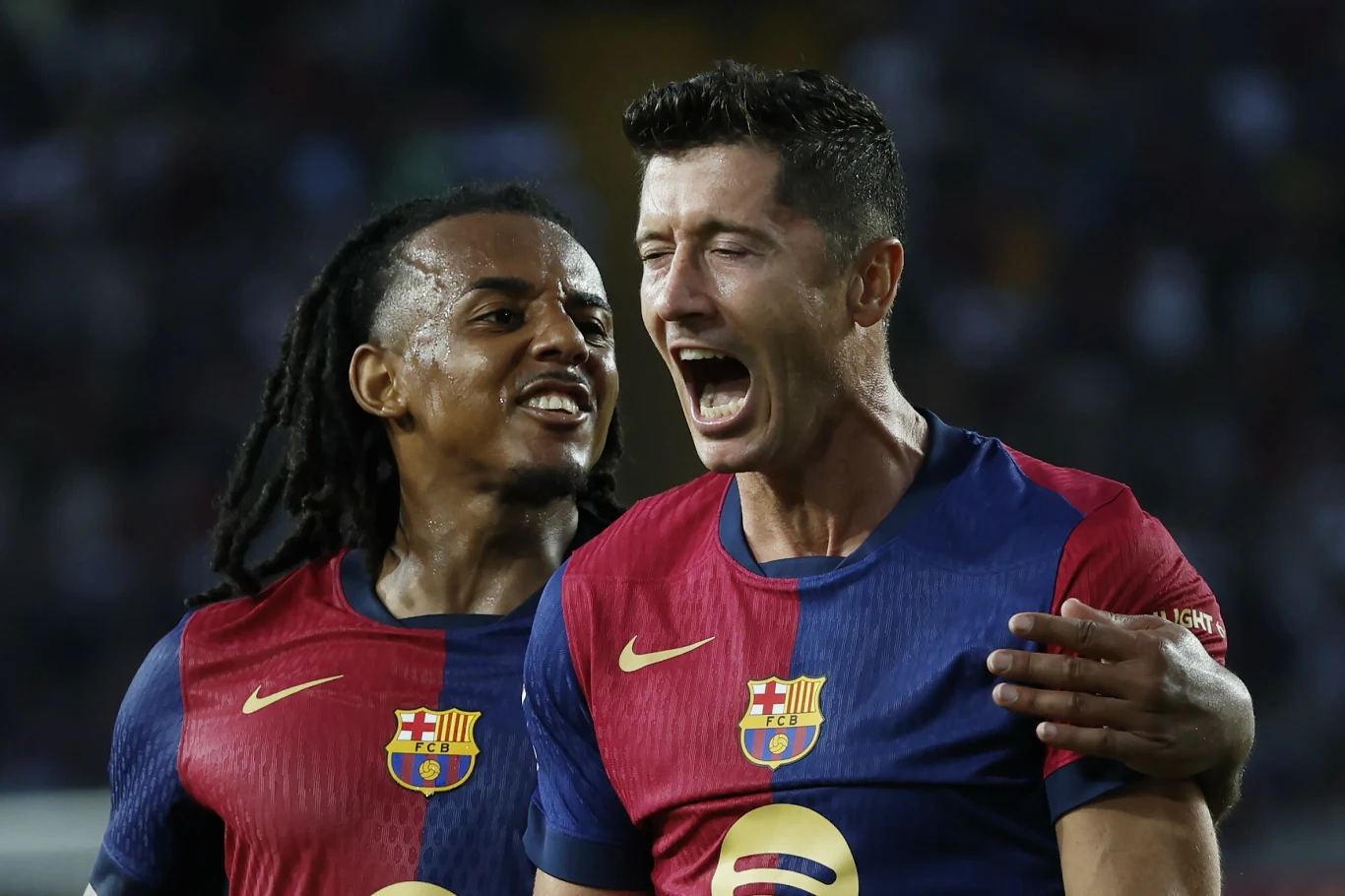 Dwóch piłkarzy FC Barcelony w granatowo-bordowych koszulkach świętuje wspólnie zdobycie bramki, jeden z nich głośno krzyczy, drugi uśmiecha się i obejmuje kolegę z drużyny.