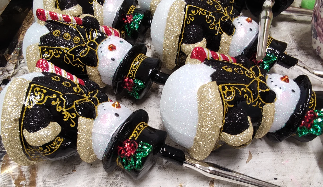 Jednym z głównych odbiorców polskich bombek choinkowych są Stany Zjednoczone Grupa brokatowych ozdób świątecznych w kształcie bałwanków w czarnych frakach z czerwono-zielonymi akcentami oraz laseczkami cukrowymi, ułożonych na białym podłożu.