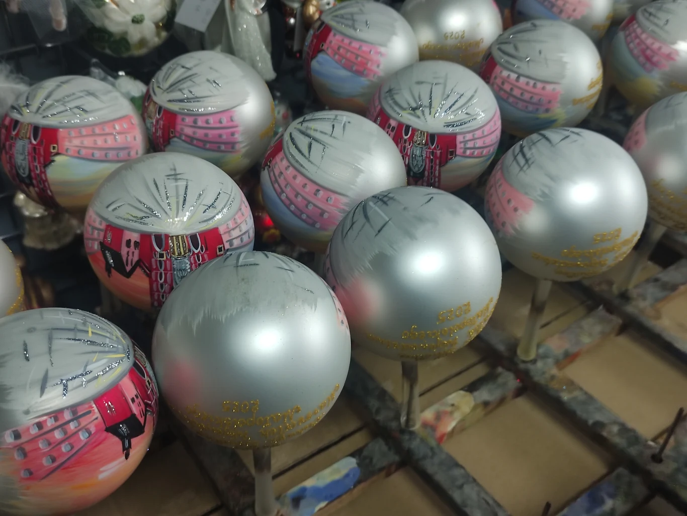 W Wieliczce trwa już pakowanie do wysyłki bombek choinkowych na 2026 rok Szereg srebrnych bombek choinkowych, częściowo pomalowanych kolorowymi wzorami, ustawionych na stojakach do schnięcia w warsztacie dekoratorskim.