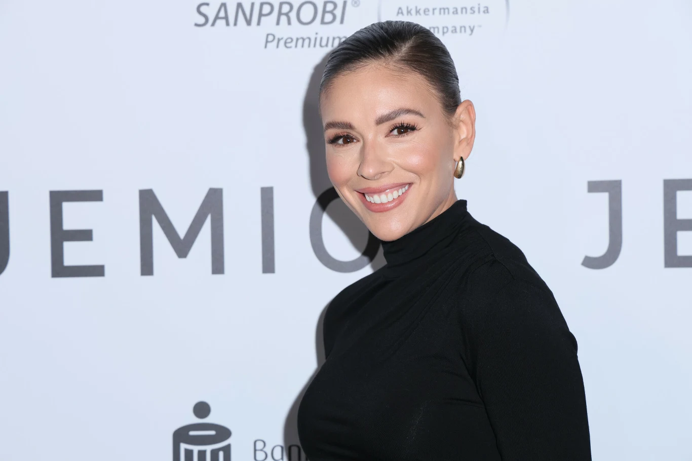 Klaudia Halejcio nie ukrywa swojego bogactwa. Jej świąteczne dekoracje kosztowały fortunę Uśmiechnięta kobieta w czarnym golfie pozuje na tle białej ścianki z logotypami i napisami.