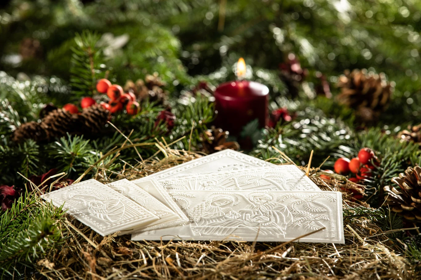 Podczas Wigilii opłatkiem dzielimy się wyłącznie w Polsce Oplatki wigilijne ułożone na sianku w otoczeniu gałązek świerku, szyszek, czerwonych owoców oraz palącej się świecy w tle, tworzącej przytulny i świąteczny nastrój.