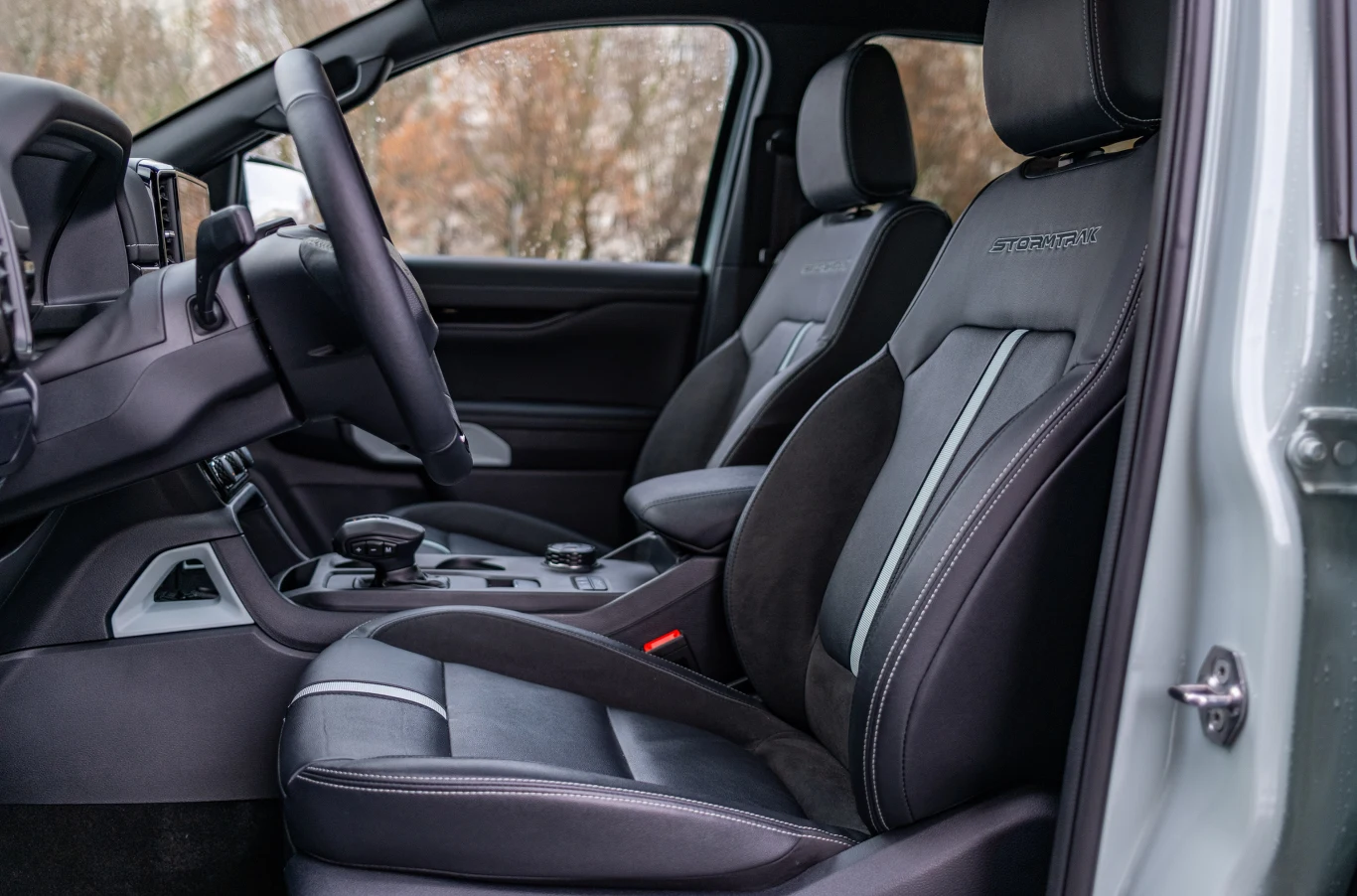 Wnętrze samochodu z widocznymi przednimi fotelami wykonanymi ze skóry i alcantary, elegancka deska rozdzielcza, nowoczesna konsola środkowa wyposażona w pokrętła i przyciski, przestronne i komfortowe miejsce kierowcy oraz pasażera.