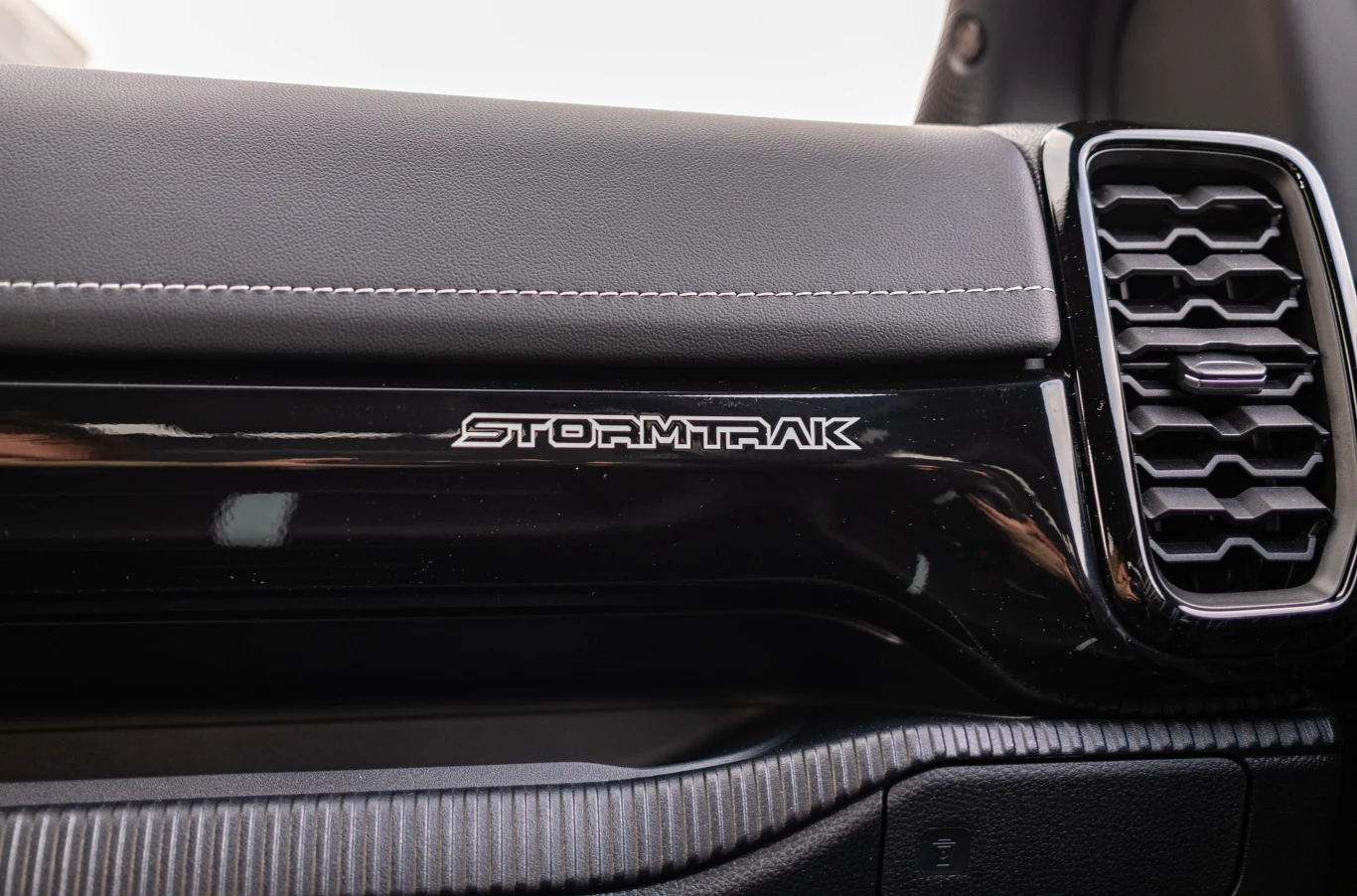 Czarny panel deski rozdzielczej z napisem STORMTRAK oraz widoczny wlot powietrza po prawej stronie, element tapicerki ze szwem i fragment wnętrza pojazdu.