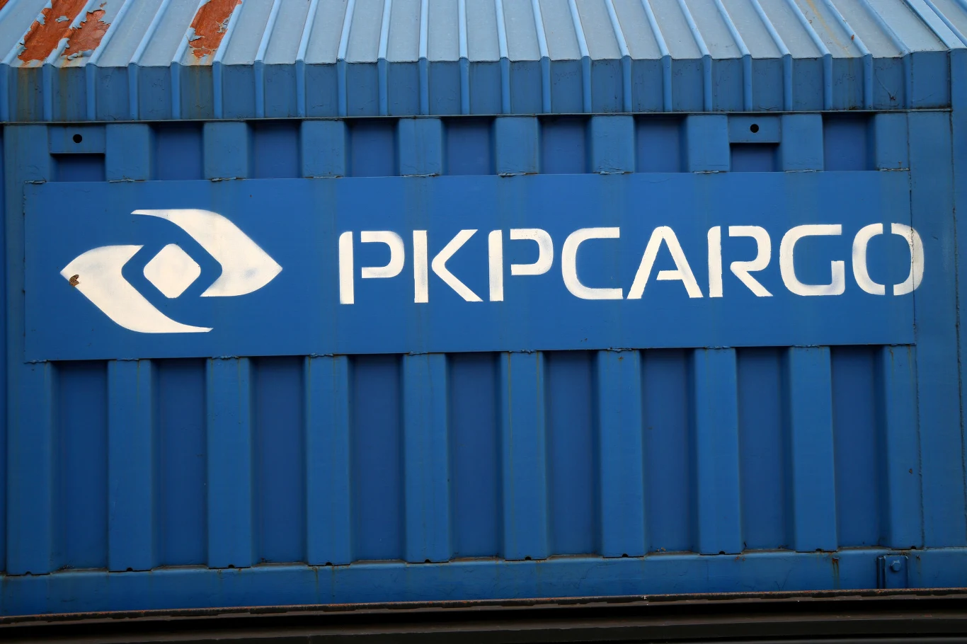 PKP Cargo złożyło pozew przeciwko Skarbowi Państwa (zdj. ilustracyjne) Niebieski kontener towarowy z dużym, białym logo PKP CARGO oraz fragmentem blachy falistej na górze, widoczne ślady rdzy przy krawędzi dachu.