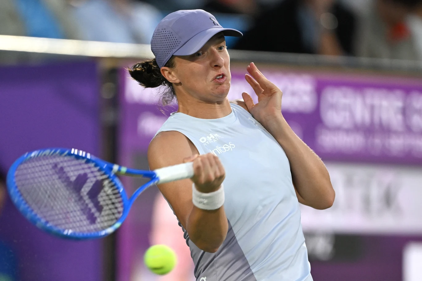 Tenisistka w jasnym stroju i czapce wykonuje uderzenie rakietą w czasie meczu na korcie tenisowym, skupienie na twarzy, piłka tenisowa widoczna przed nią.