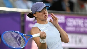 Tenisistka w jasnym stroju i czapce wykonuje uderzenie rakietą w czasie meczu na korcie tenisowym, skupienie na twarzy, piłka tenisowa widoczna przed nią.