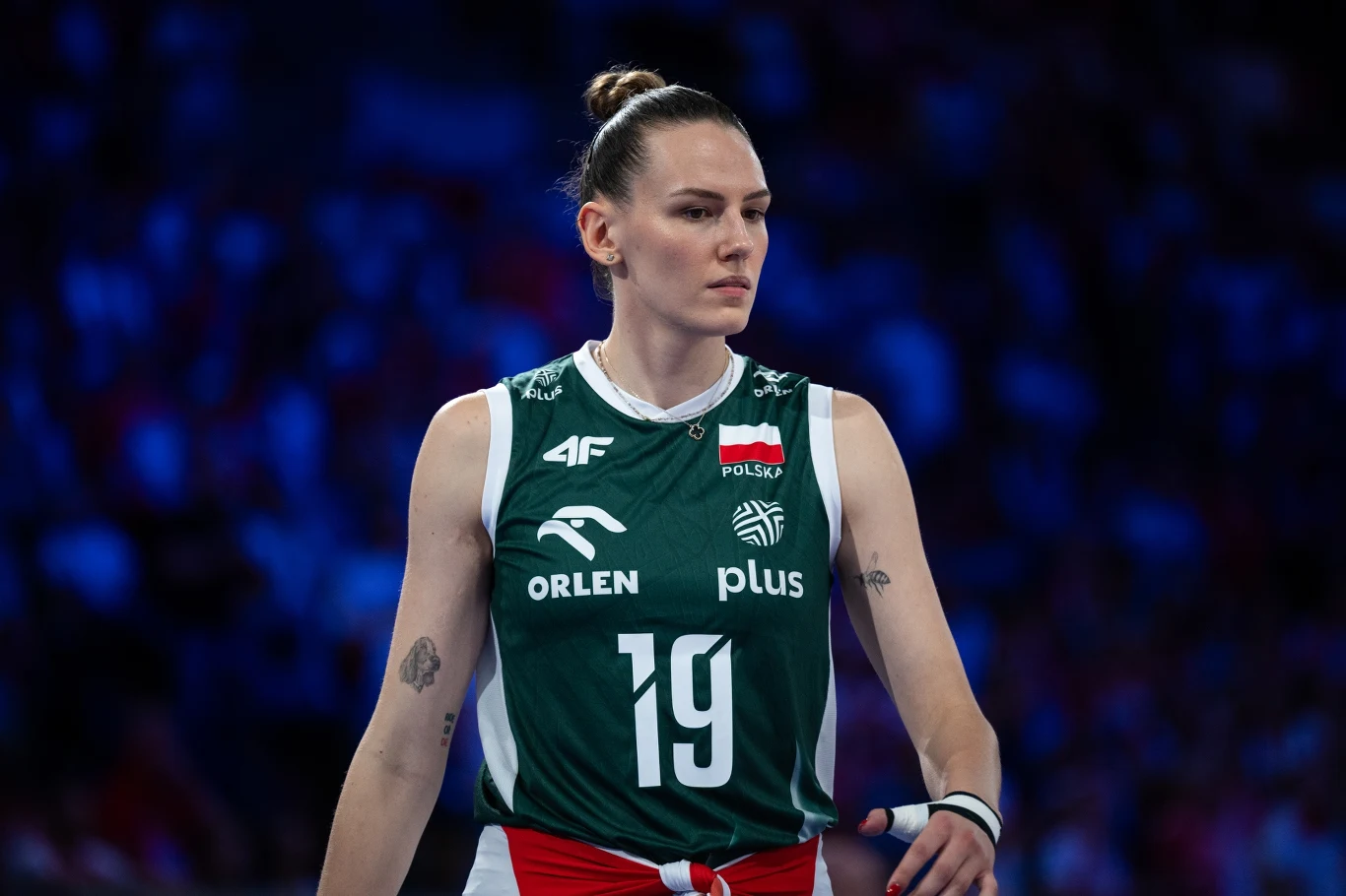Siatkarka w zielonym stroju reprezentacji Polski z numerem 19, skupiona podczas meczu, widoczna na tle rozmytego, niebieskiego tłumu na trybunach.
