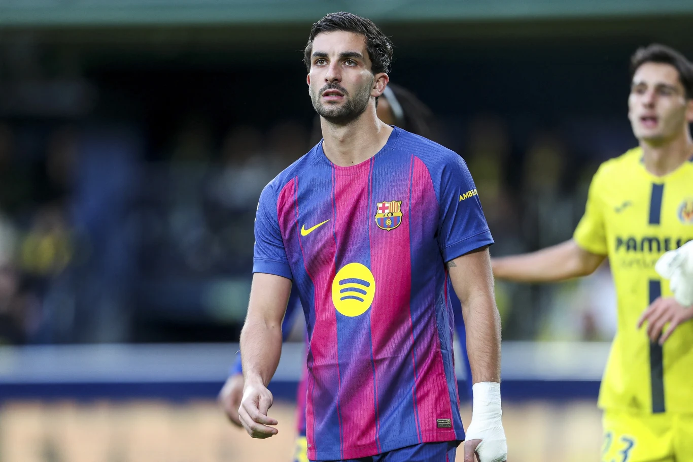 Piłkarz w koszulce FC Barcelony na boisku podczas meczu, na drugim planie zawodnik drużyny w żółtych strojach.