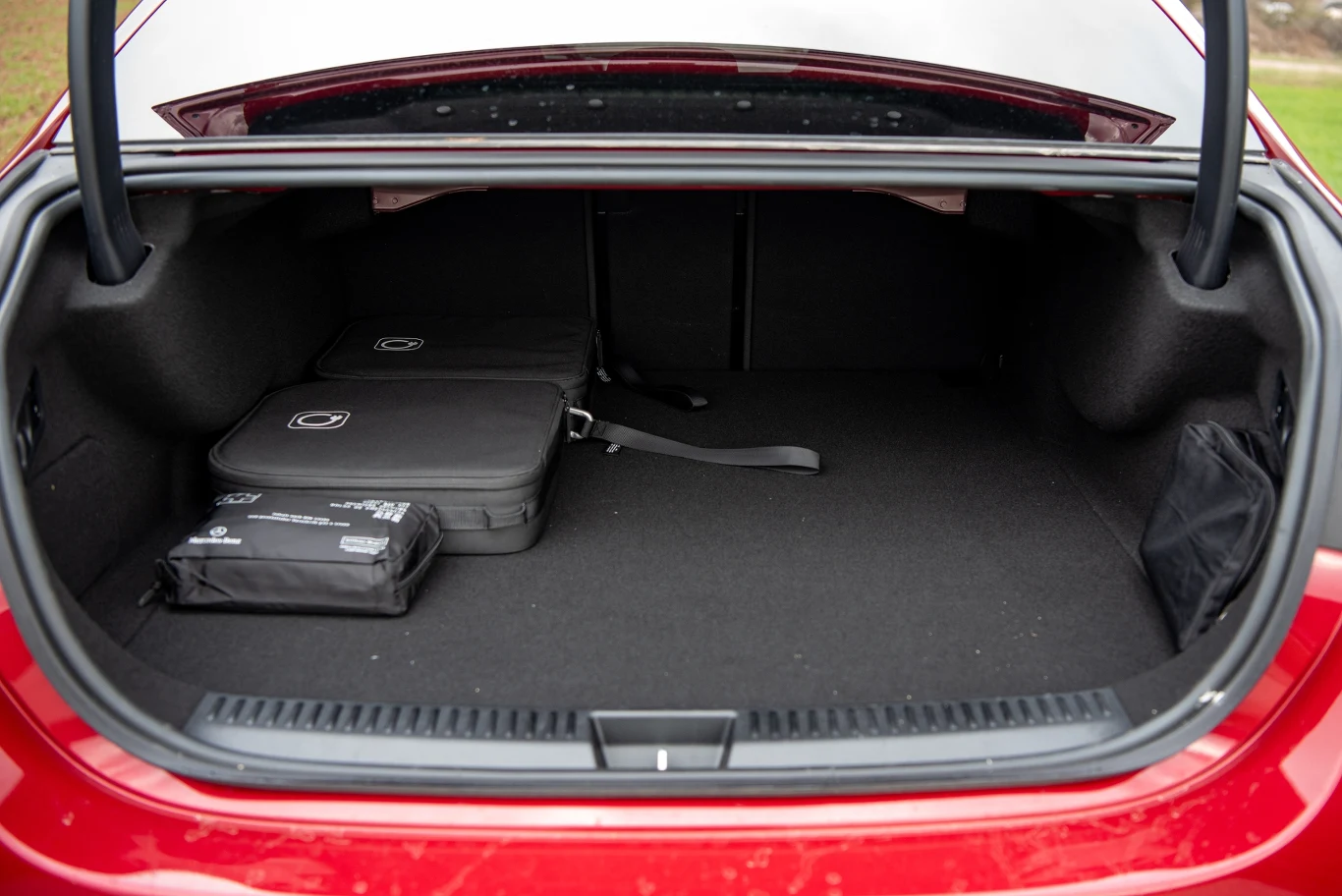 Otwarty bagażnik czerwonego samochodu, w którym znajdują się dwie torby oraz apteczka. Przestrzeń jest czysta i dobrze uporządkowana.