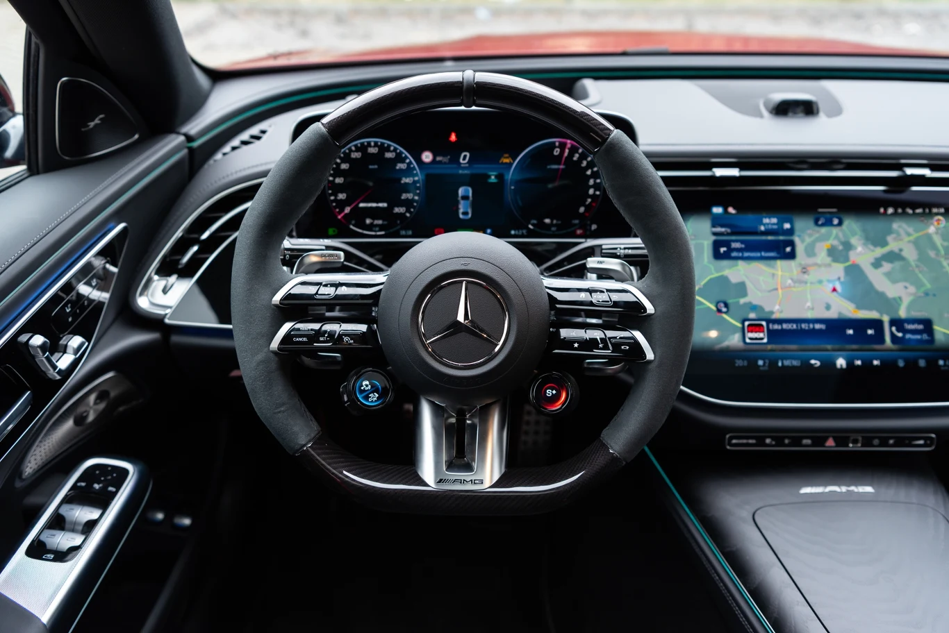 Kierownica samochodu marki Mercedes-AMG z wielofunkcyjnymi przyciskami, cyfrowy zestaw wskaźników oraz ekran nawigacji wielkoformatowej po prawej stronie kokpitu.