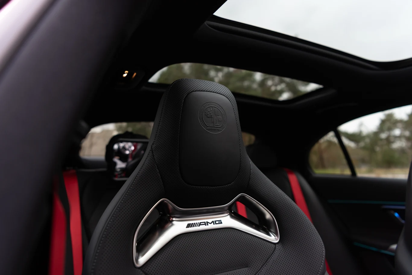 Sportowy fotel AMG w luksusowym samochodzie z czerwonymi pasami bezpieczeństwa, panoramicznym dachem oraz nowoczesnym wykończeniem wnętrza.