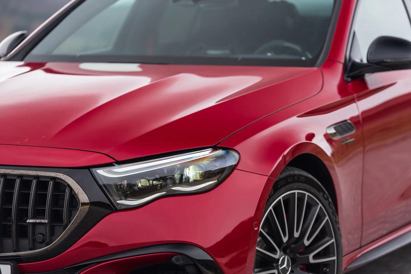 Czerwony samochód klasy premium z nowoczesnymi reflektorami LED, wyraźnie widocznym przednim grillem i eleganckimi, sportowymi felgami. Sylwetka auta podkreślona metalicznym lakierem oraz detalami wykończenia.