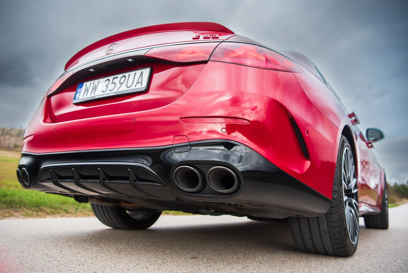 Czerwony sportowy samochód widziany z niskiej perspektywy od tyłu, charakterystyczne cztery rury wydechowe, czarne felgi i polska tablica rejestracyjna na tle pochmurnego nieba.