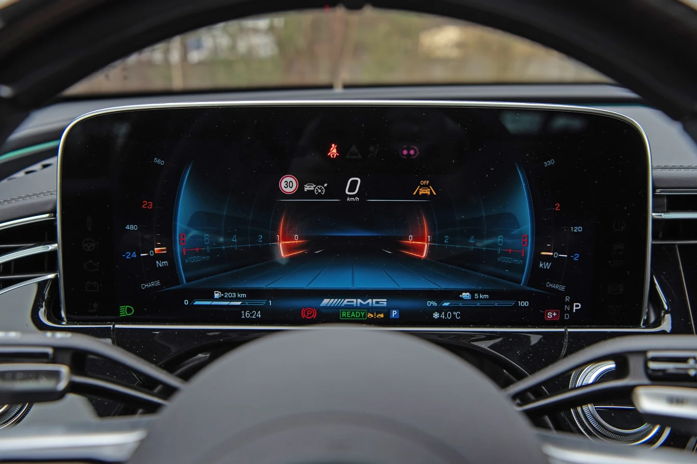 Cyfrowy kokpit samochodowy z widocznym kolorowym ekranem, który wyświetla m.in. informacje o prędkości, ograniczeniach prędkości, tempie jazdy, wskaźnikach systemu, ustawieniach klimatyzacji oraz logo AMG.