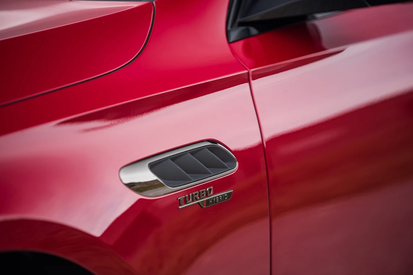 Czerwony błyszczący bok samochodu z wyraźnym emblematem TURBO oraz chromowanym wlotem powietrza obok drzwi kierowcy.