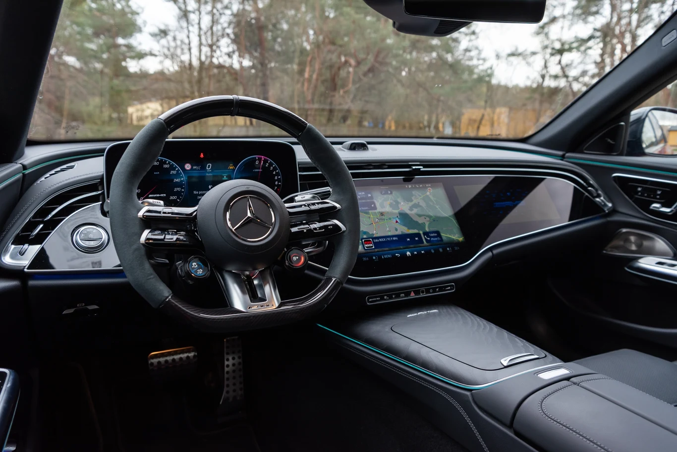 Luksusowe wnętrze samochodu marki Mercedes, nowoczesna deska rozdzielcza z dużym wyświetlaczem, wysokiej klasy kierownica i cyfrowe zegary, jasne oraz przestronne wykończenie, widoczna nawigacja oraz detale wysokiej jakości.