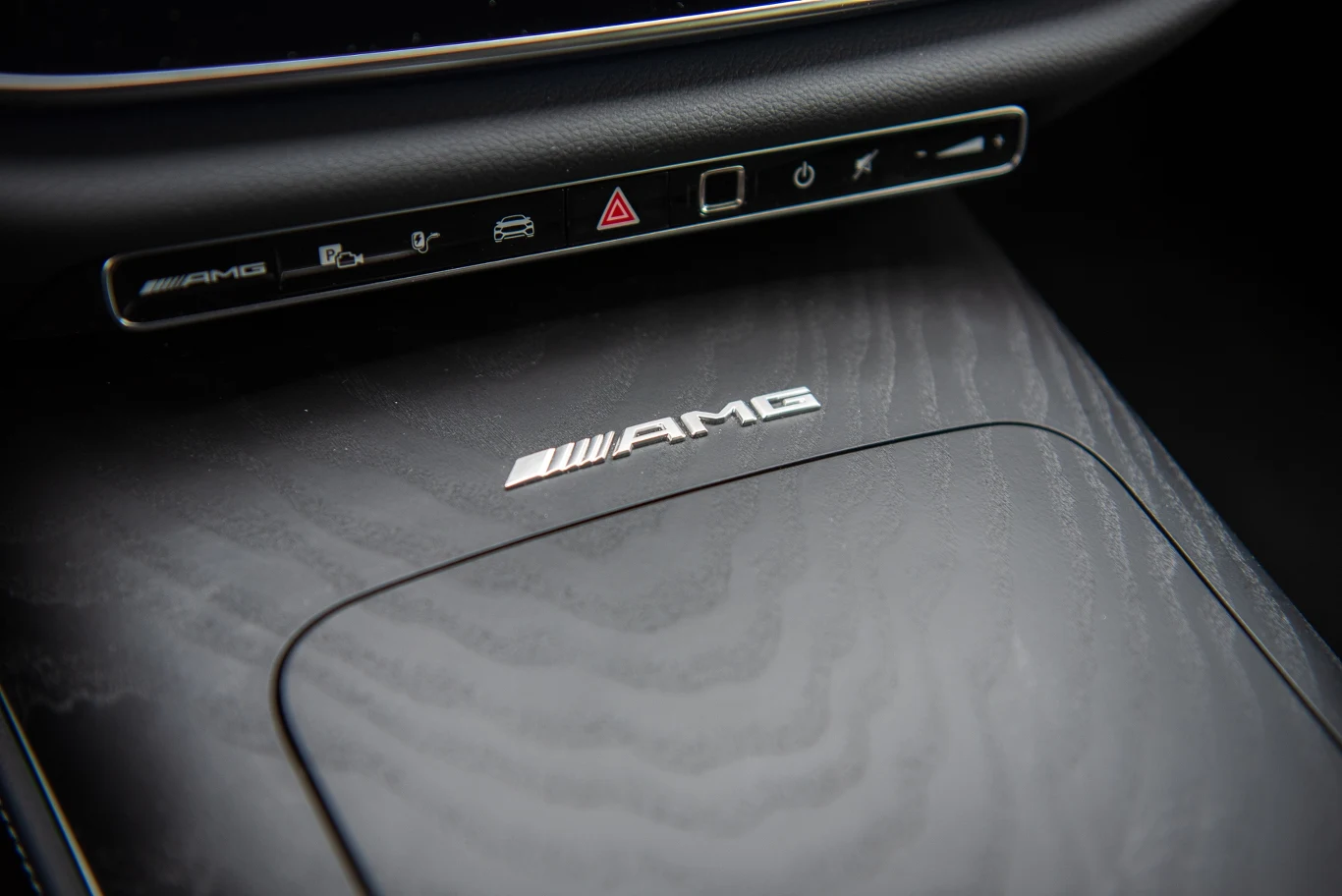 Panel środkowy samochodu z logo AMG, widoczne przyciski sterujące oraz eleganckie wykończenie powierzchni.