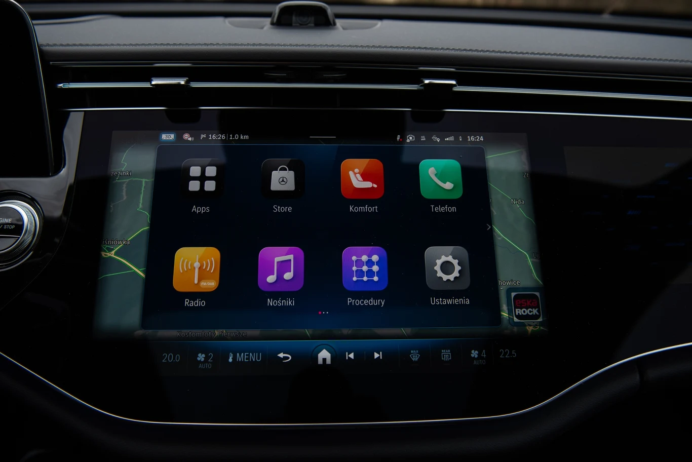 Centralny wyświetlacz samochodu z widocznym interfejsem systemu multimedialnego, wyświetlającego różne ikony aplikacji takie jak radio, nawigacja, telefon oraz ustawienia, w ciemnym, nowoczesnym wnętrzu pojazdu.