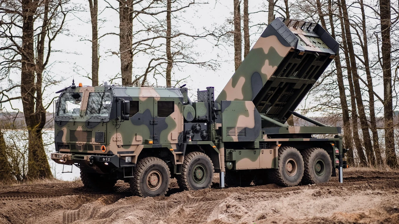 Wieloprowadnicowa wyrzutnia rakietowa na ciężarówce wojskowej w kamuflażu, ustawiona w leśnym terenie, uniesiona platforma gotowa do odpalenia pocisków