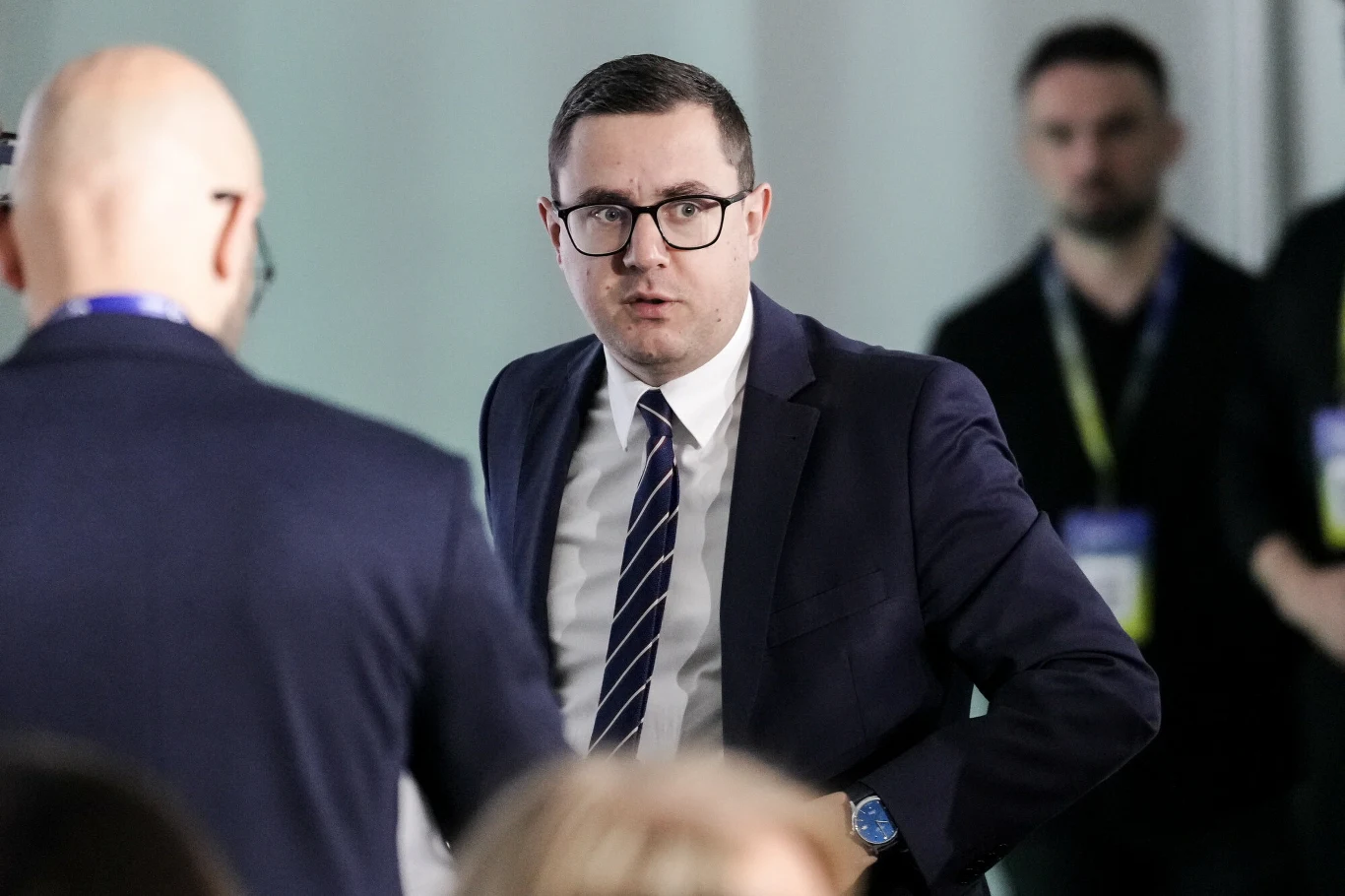 Minister energii Miłosz Motyka: Jeżeli sytuacja będzie rozwijała się w sposób skrajnie negatywny to nie wykluczamy tymczasowego obniżenia stawki VAT na paliwo Minister energii Miłosz Motyka w garniturze i okularach podczas oficjalnego wydarzenia z innymi uczestnikami.