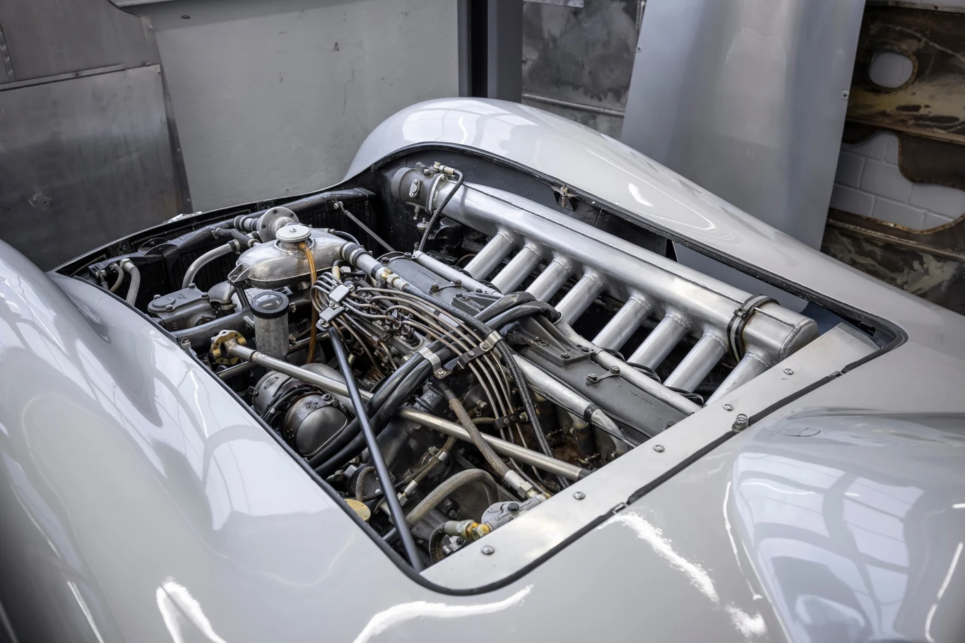 Komora silnika klasycznego samochodu sportowego z widocznym, rozbudowanym układem mechanicznym oraz licznymi elementami metalowymi; maska pojazdu jest otwarta, eksponując szczegółowe detale silnika.