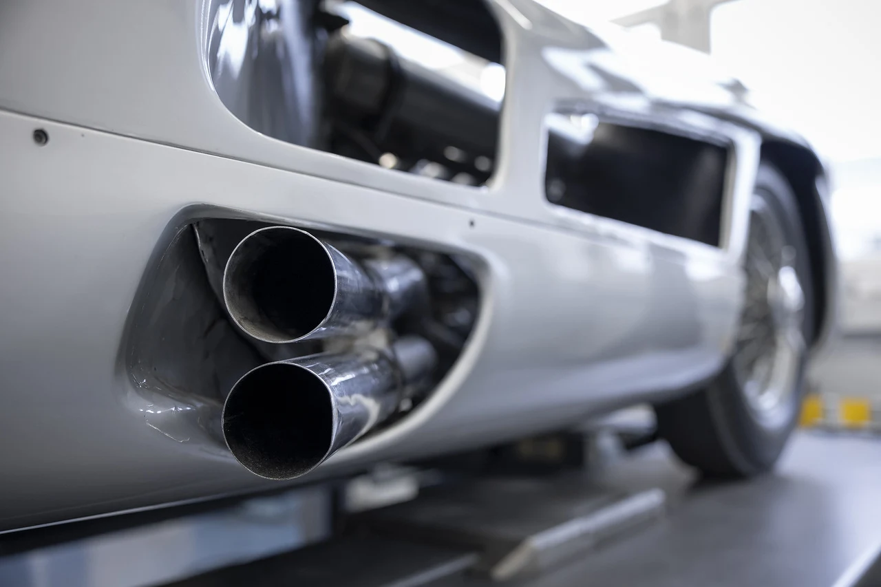 Metaliczne rury wydechowe sportowego samochodu z połyskującą karoserią, ujęcie z bliska, skoncentrowane na detalach technologicznych. W tle fragment tylnego koła oraz odbicia światła na powierzchni pojazdu.